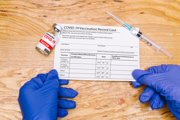 The coronavirus vaccination card is held by a doctor at the table with a vaccine and a syringe