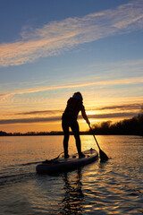Silhouette of a woman on Stand Up Paddle Board (SUP) at sunset in winter river