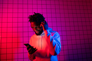the concept of music. A black man listens to music with headphones on against a background of neon light. Red and blue background