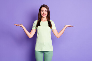 Photo portrait of cheerful girl keeping empty spaces on both palms isolated on vivid violet color...