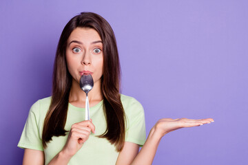 Photo portrait of young girl licking spoon staring keeping empty space on hands isolated on vivid...