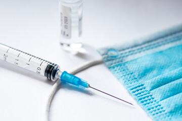 Syringe with needle, vial and surgical face mask on a black table ready to be used. Covid or Coronavirus vaccine background