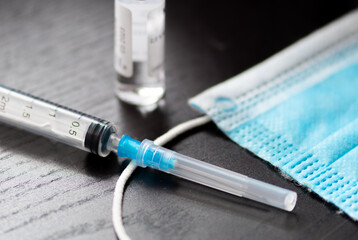 Syringe, vial and surgical face mask on a black table ready to be used. Covid or Coronavirus...