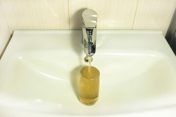Dirty tap water flows out of the mixer. A glass cup filled with muddy water is in the sink.