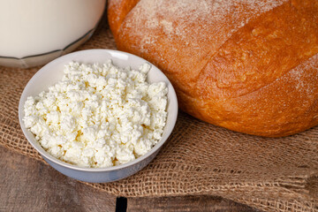Glass jar of milk, bowl of cottage cheese and bread on wooden table