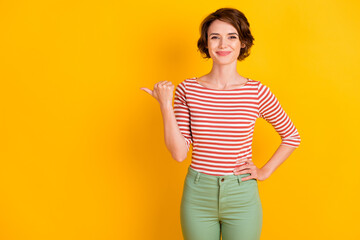 Portrait photo of girl with bob hair pointing at empty space smiling isolated on vivid yellow color background