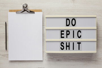 'Do epic shit' on a lightbox, clipboard with blank sheet of paper on a white wooden surface, top view. Flat lay, overhead, from above.