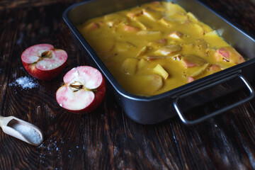 Making an apple pie. Raw dough in a baking dish, apple and sugar on the wooden table
