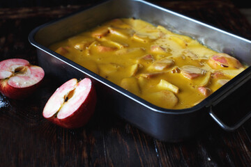 Making an apple pie. Raw dough in a baking dish, apple and sugar on the wooden table