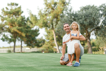 Portrait of a happy caring father teaching his small pretty daughter how launching a toy plane in a green park ,smiling full length