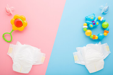 White baby diapers, soothers, bear with balls and flower rattle on light pink blue table background. Pastel color. Closeup. Top down view.