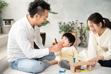 Obraz premium 新築の様な白くて広い部屋でイケメンの旦那さんが赤ちゃんをあやす家族団らんの幸せな若いファミリー