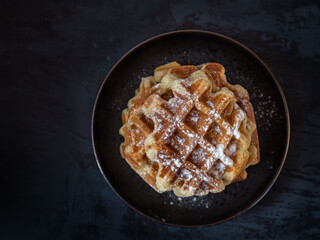 Homemade waffles with powdered sugar on a round black plate