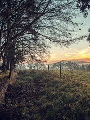 A frozen misty field at sunrise. The layers mist settle over the lower ground across a classic British countryside view at sunrise in winter.