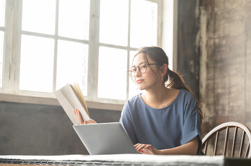 パソコンと本を開いて調べながら仕事をする美しい眼鏡の似合う日本人女性4　バストアップ煽り広角
