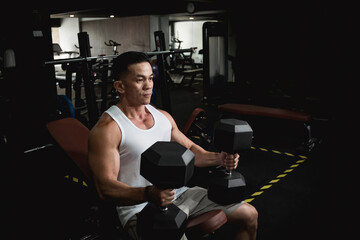 An athletic asian man lift some heavy hex dumbbells, preparing mentally to work out chest and...