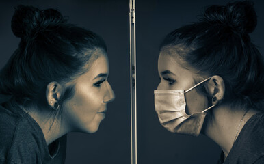 Composing a young pretty woman with a respirator sees her likeness without a mask behind a safety window.