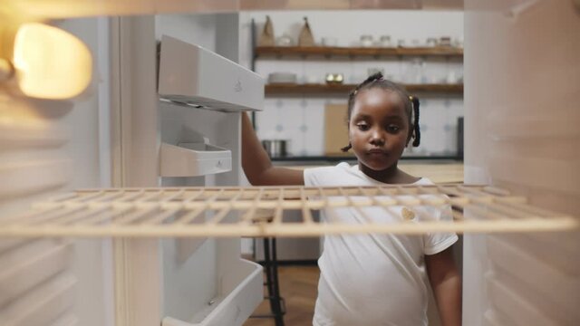Hungry poor little african girl look for food in empty fridge at home.