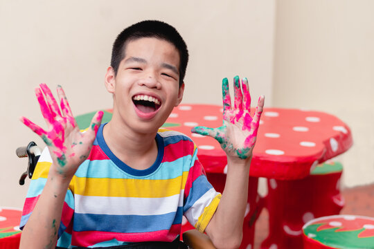 Asian disabled child on wheelchair smiling with his hands were stained with watercolor, Skills to practice muscle development,Lifestyle in education age of special kids, Happy disability kid concept.
