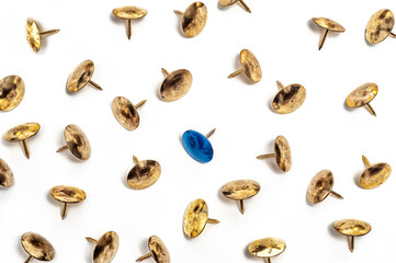 Single blue thumbtack among many brass colored ones on white background