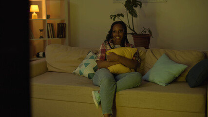 Smiling young african woman relaxing on couch at home watching tv