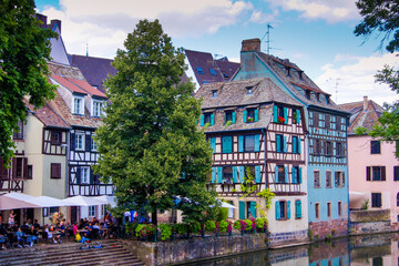 Fototapeta na wymiar Colorful half-timbered houses and a restaurant with an outdoor area at a canal in the historical city of Strasbourg. The house facades reflect in the water.