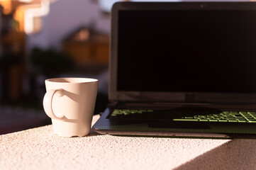 Cup of coffee and computer in the sun