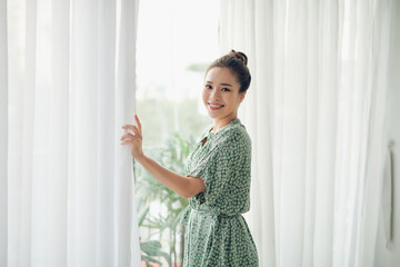 Young woman opening curtains in morning