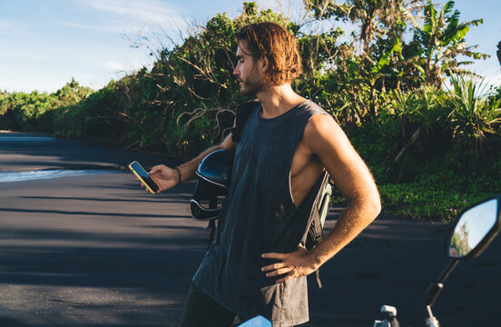 Young male hipster using smartphone on sandy road