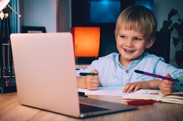 School boy with laptop at table in evening at home.