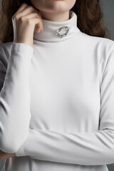 Cropped shot of brown-haired lady with elegant brooch on the collar of her white roll-neck jumper....