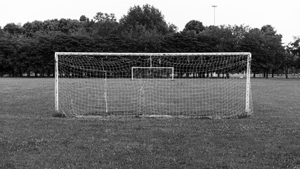 Abandoned soccer field in a Milan park, Italy. Damaged football net. Monochrome