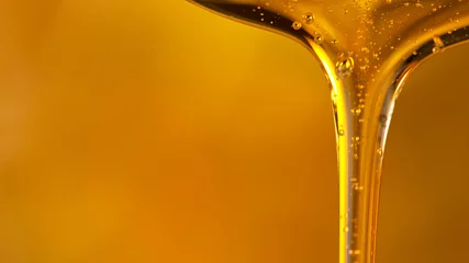 Fotobehang Pouring oil or honey drop on golden background. Macro shot. © Lukas Gojda