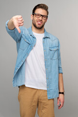 Portrait of young handsome caucasian man in jeans shirt showing big thumb down dislike gesture...