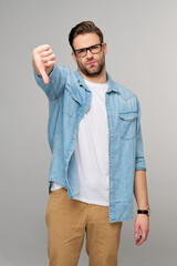 Portrait of young handsome caucasian man in jeans shirt showing big thumb down dislike gesture...