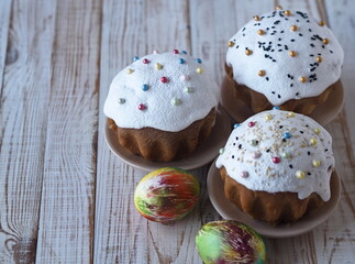 Sweet muffins, with cream and festive sprinkles, baked for the Orthodox Christian holiday of Easter with colored eggs on a light background.