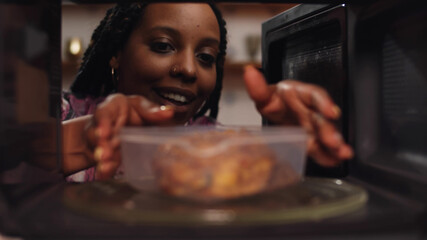 Afro-american woman using the microwave oven to heating food.