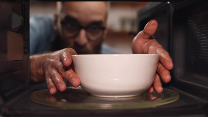 Young caucasian man heating food in microwave oven