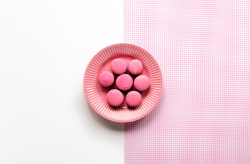 Pink macaroons on a plate. Simple monochrome flat lay on split two tone pink white background. Creative food concept.