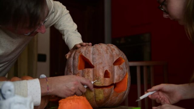4K Father and daughter carving pumpkin, Jack o lanterns on Halloween in the kitchen. Celebrating Halloween at home with a Creepy Pumpking, fall family tradition