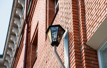 Fototapeta na wymiar Lantern on the wall of a red brick building. Elements of urban architecture. View from below