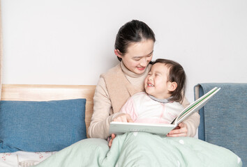 Mother and daughter sit on the bed reading together