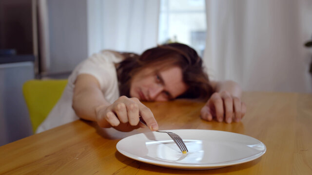 Anorexic young man consciously choosing severe diet having corn grain on plate