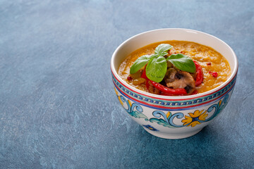 A bowl of pumpkin cream soup on blue background with copy space.