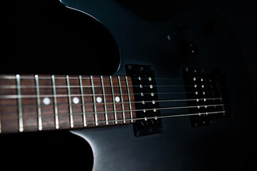 Naklejka na ściany i meble Black electric guitar on a dark background with backlit strings
