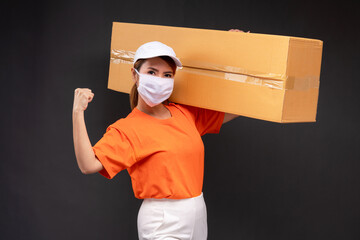 Delivery asian woman or courier wearing an orange masked uniform holds a cardboard box and act...