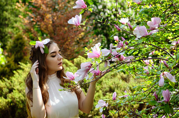 Portrait of young attractive woman in spring garden with blooming magnolias. Spring background. Woman's Day. Greeting card. 
