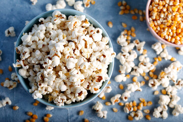 Fototapeta na wymiar Salty popcorn in a blue bowl with corncobs on the blue background.