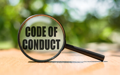 Magnifying glass with text CODE OF CONDUCT on wooden table and green background.