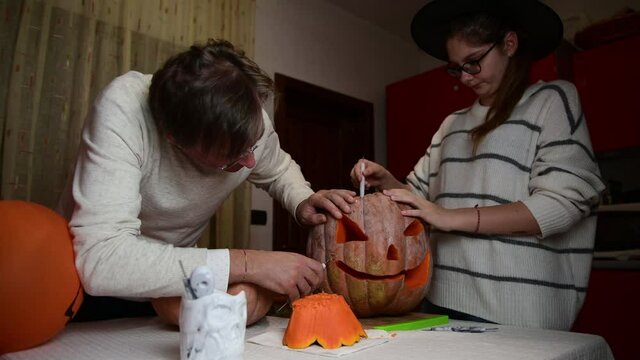 4K Father and daughter carving pumpkin, Jack o lanterns on Halloween in the kitchen. Celebrating Halloween at home with a Creepy Pumpking, fall family tradition